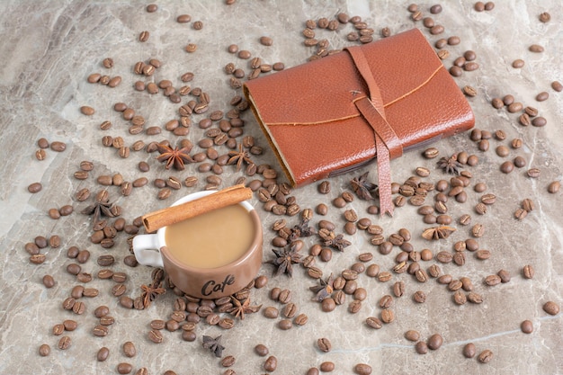 Tasse Milchkaffee mit Kaffeebohnen und Notizbuch.