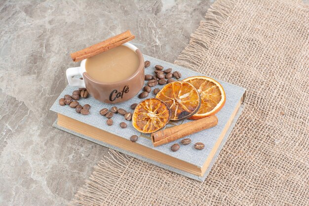 Tasse Milchkaffee mit Kaffeebohnen und Orangenscheiben auf Buch.