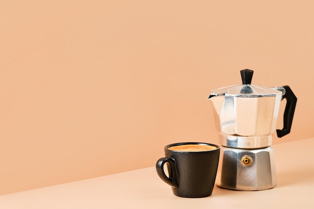 Tasse mit Espressokaffee und Kaffeekanne auf farbigem Hintergrund mit Kopierplatz für Text. Kaffeeidee im italienischen Stil zum Frühstück. Kaffee mit Schaum in einer schwarzen Tasse.