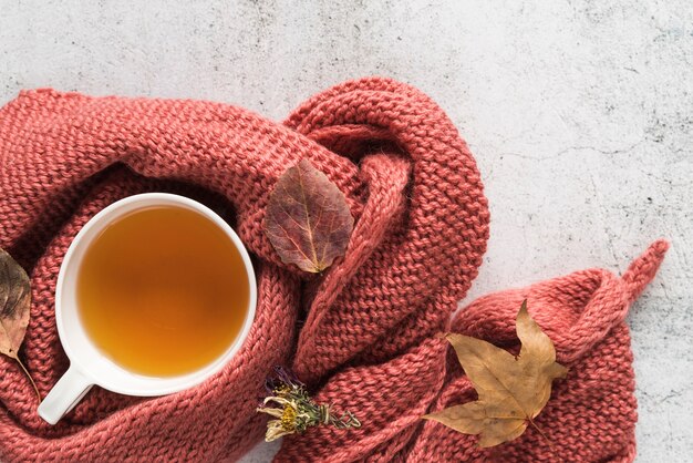 Tasse mit Getränk in Strickwaren und Blätter