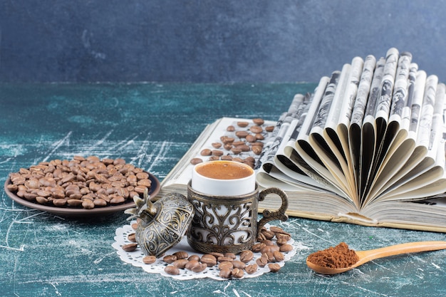 Tasse schaumigen Kaffee, Teller mit Kaffeebohnen und Buch auf Marmortisch.