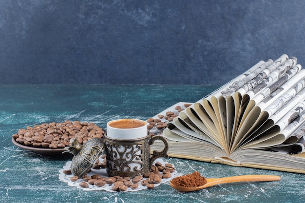 Kostenloses Foto tasse schaumigen kaffee, teller mit kaffeebohnen und buch auf marmortisch.