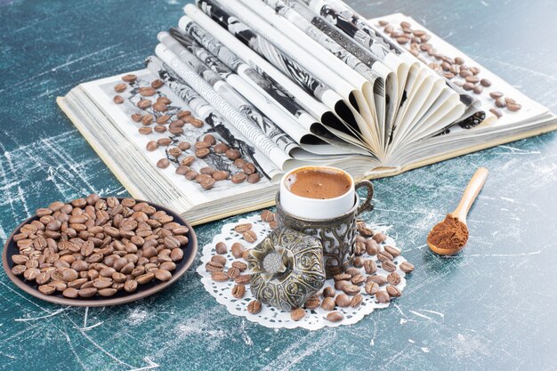 Tasse schaumigen kaffee, teller mit kaffeebohnen und buch auf marmortisch.