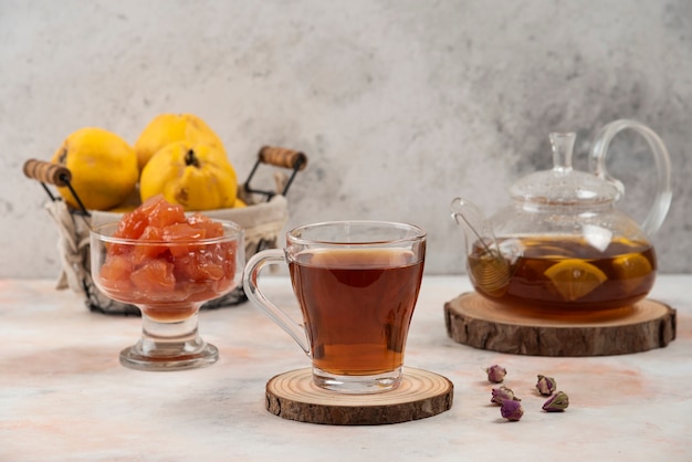 Tasse schwarzer Tee, Quittenfrucht und Marmelade auf Marmortisch.