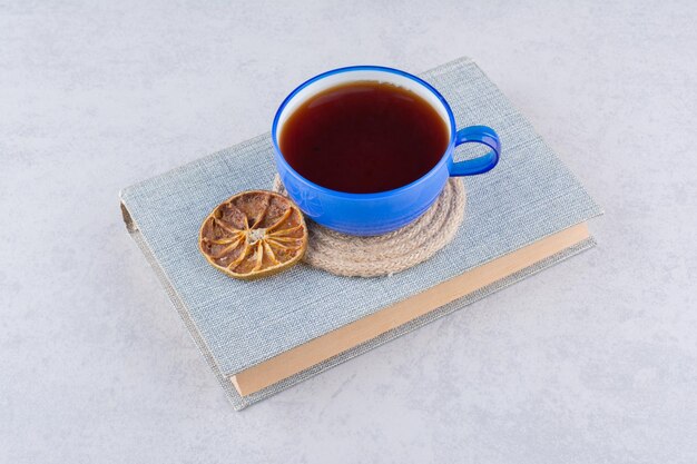 Tasse Tee auf Buch mit Orangenscheibe. Foto in hoher Qualität