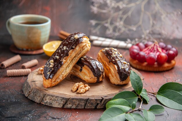 Tasse Tee der Vorderansicht mit köstlichen Schoko-Eclairs auf dunklem Hintergrund