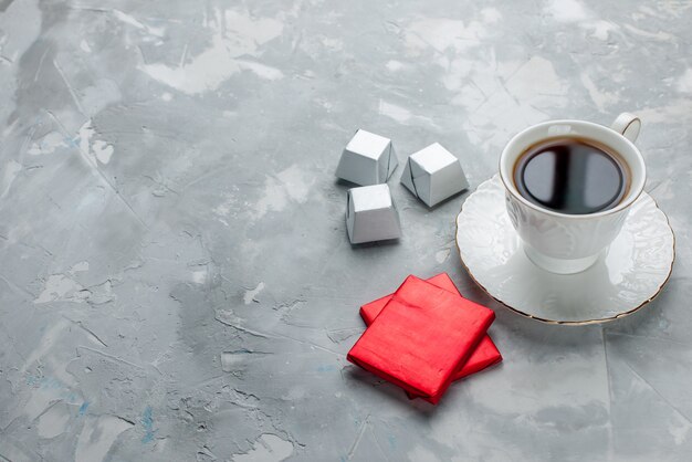 Tasse Tee heiß in weißer Tasse auf Glasplatte mit Silberverpackung Pralinen auf hellem Schreibtisch, Tee trinken süße Schokolade Keks Teatime