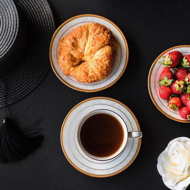 Tasse Tee mit Brot und Erdbeere auf schwarzem Hintergrund