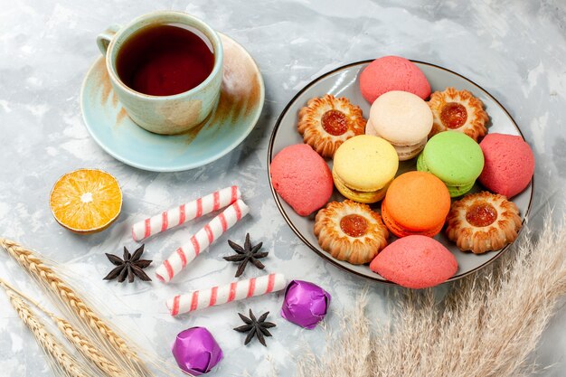 Tasse Tee mit halber Draufsicht mit Keksen und französischen Macarons auf hellweißem Oberflächenbonbon, süßem Zuckerkuchen, Backkeks