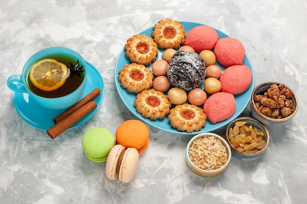 Tasse tee mit halber draufsicht mit keksen und kuchen von french macarons auf weißer oberfläche