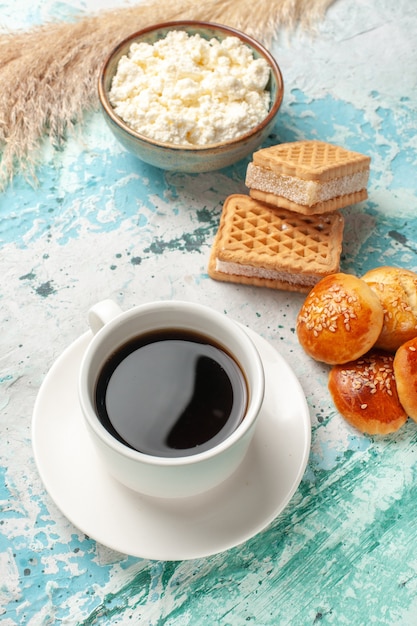 Tasse Tee mit halber Draufsicht, Waffeln und kleinen Kuchen auf blauer Oberfläche