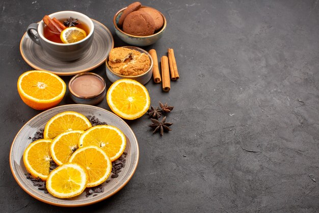 Tasse Tee mit Keksen und frisch geschnittenen Orangen im Dunkeln