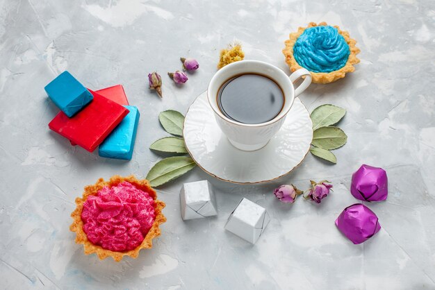 Tasse Tee mit rosa Sahnekuchen Pralinen auf hellem Schreibtisch, Keks süße Teesüßigkeiten