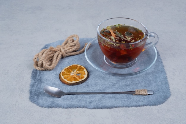 Tasse Tee, Seil und getrocknete Orangenscheibe auf Tischdecke.