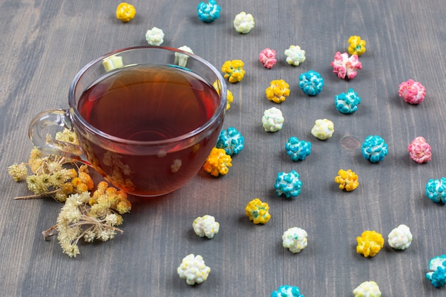 Tasse tee, trockenblumen und buntes popcorn auf holzoberfläche