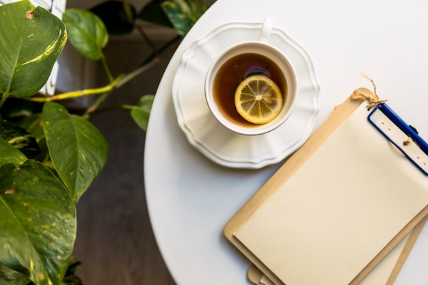 Tasse Tee und leeres Papier befestigen Sie am Klemmbrett über dem weißen Schreibtisch