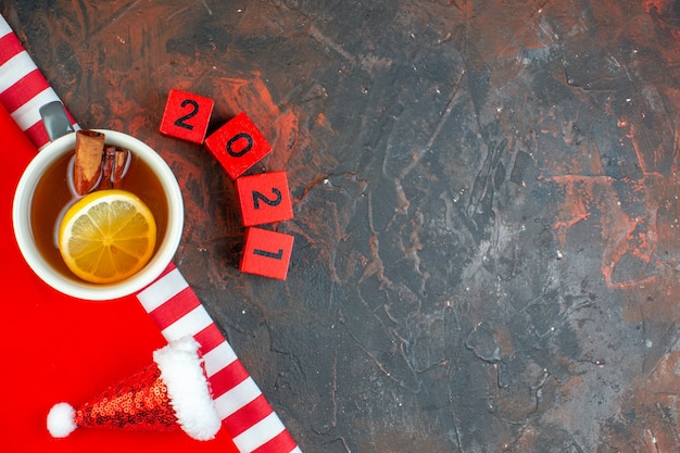 Kostenloses Foto tasse tee von oben, aromatisiert mit zitrone und zimt, mini-weihnachtsmütze auf roten tischdecken-holzblöcken auf dunkelrotem tisch mit freiem platz