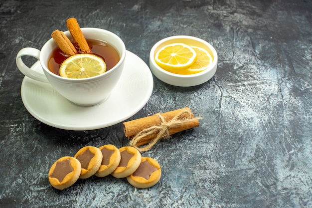 Tasse Tee von unten, aromatisiert mit Zitronen- und Zimtzitronenscheiben in kleinen Untertassenkeksen, gebundene Zimtstangen auf dunklem Tischfreiraum