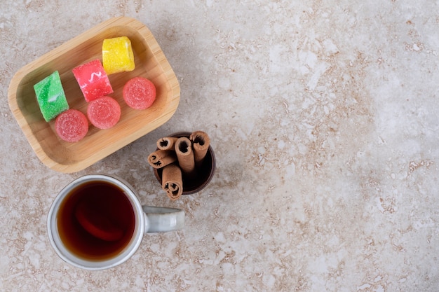 Tasse tee, zimtstangen und marmeladenbonbons auf marmoroberfläche
