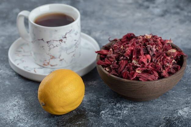 Tasse Tee, Zitrone und Schüssel mit getrockneten Blumen auf Marmortisch.