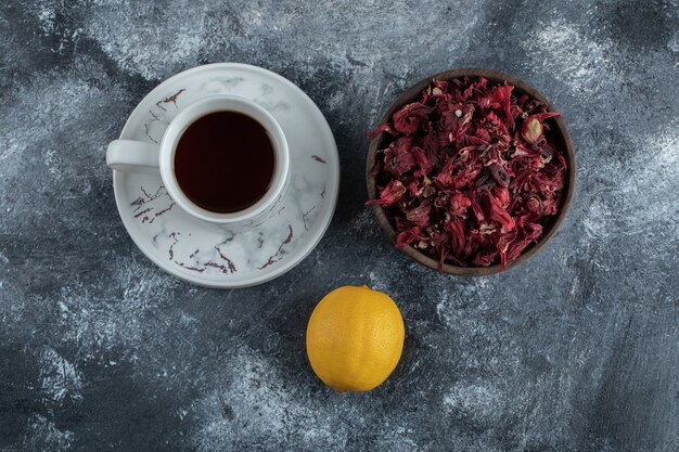 Tasse Tee, Zitrone und Schüssel mit getrockneten Blumen auf Marmortisch.