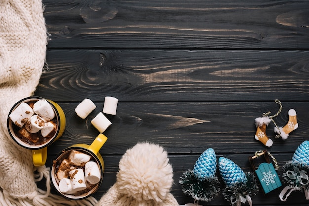 Tassen mit Marshmallows in der Nähe von warmer Kleidung und Weihnachtsspielzeug