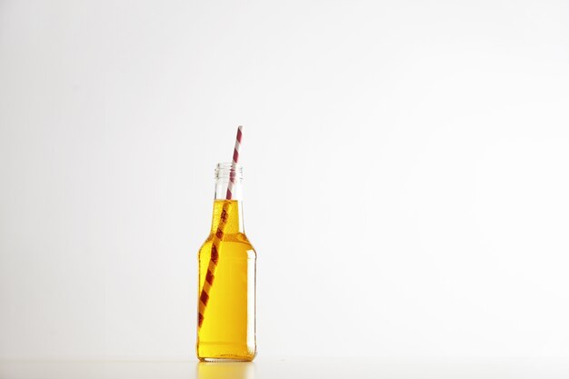 Tastu funkelndes gelbes Getränk mit rot gestreiftem Trinkhalm in geöffneter rustikaler Glasflasche lokalisiert auf Weiß
