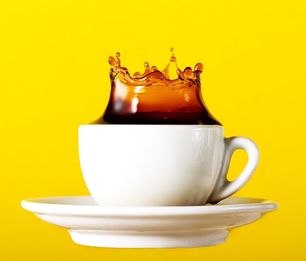 Tasty frischen schwarzen Kaffee in Tasse splash Krone auf gelb lebendigen Hintergrund. Kunstdesign