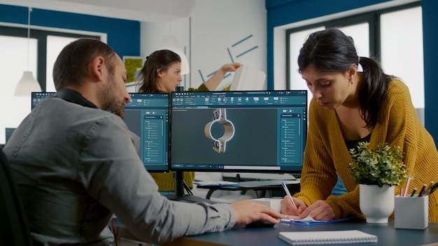 Kostenloses Foto team diskutiert über industrieprojekt mit dual-monitor-setup zum entwerfen von zahnrädern und metallkla...