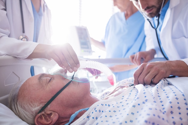 Kostenloses Foto team von ärzten, die sauerstoffmaske auf ein männliches älteres patientengesicht setzen