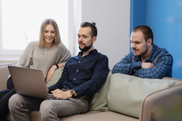 Team von drei Personen, die am Laptop im Büro auf dem Sofa arbeiten