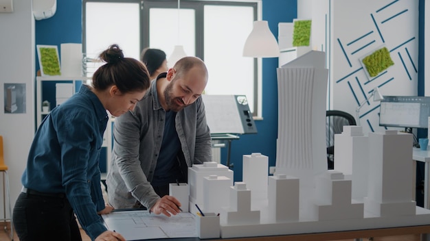 Team von Kollegen, die das Gebäudemodell als Inspiration für die Gestaltung des Baulayouts verwenden. Mann und Frau, die mit Maquette arbeiten, um Blaupausen und Stadtstrukturen zu planen. Architekturprojekt