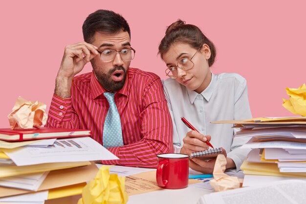 Teamwork-Konzept. Junge Mitarbeiter in großen Gläsern Brainstrom zusammen, studieren Dokumente für zukünftige Geschäftsabschlüsse, schreiben Notizen in Spiralblock