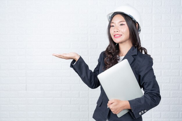 Technikfrau, die ein unterschiedliches Notizbuch, weiße Backsteinmauer hält Machte Gesten mit Gebärdensprache.