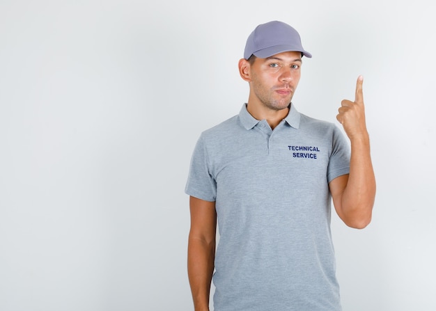 Technischer Servicemann, der Finger oben im grauen T-Shirt mit Kappe zeigt