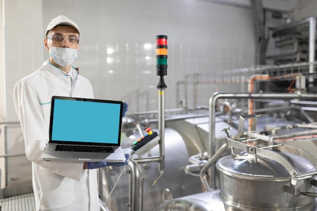 Technologe im weißen Kittel mit Laptop in den Händen kontrolliert den Produktionsprozess im Molkereigeschäft Ort zum Schreiben Technologe mit Laptop-Computer ist in der Fabrik