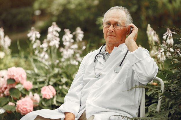 Technologie-, Menschen- und Kommunikationskonzept. Älterer Mann im Sommerpark. Doktor mit einem Telefon.