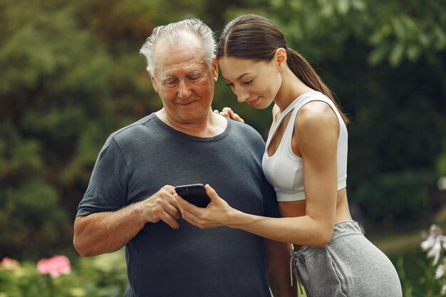 Technologie-, Menschen- und Kommunikationskonzept. Älterer Mann im Sommerpark. Großvater mit Enkelin.