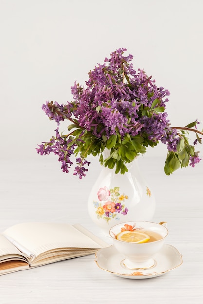 Tee mit Zitrone und Bouquet von lila Primeln auf dem Tisch