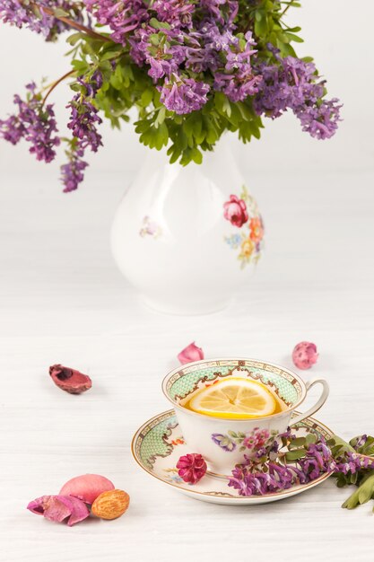 Tee mit Zitrone und Bouquet von lila Primeln auf dem Tisch