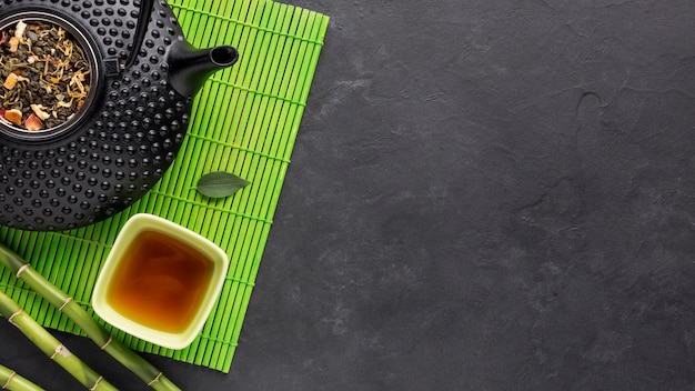Tee und trockene Kräuter auf grünem Tischset über schwarzer Oberfläche