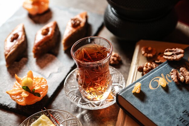 Tee von der Seite in einem Armudu-Glas mit Baklava und einem Buch auf dem Tisch