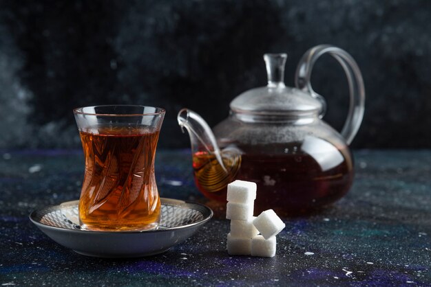 Teekanne und Glas Tee mit Zucker