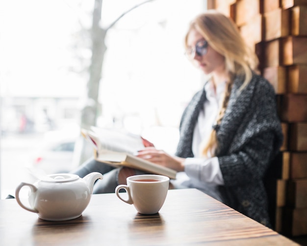 Teekanne und Tasse, die nahe Lesefrau steht