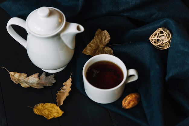 Teekanne und Tasse in der Nähe von Blättern und Draperie