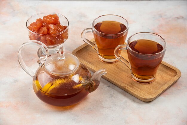 Teekanne und Tassen schwarzer Tee und Quittenmarmelade auf Holzplatte.