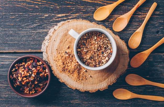 Teekräuter in einer Schüssel und Tasse mit Löffeln Draufsicht auf einem Holzstummel und dunklem hölzernem Hintergrund