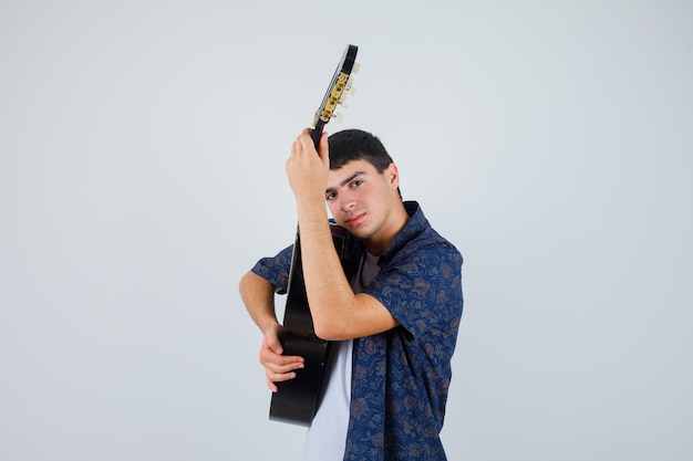 Teen Boy hält Gitarre auf der Brust im T-Shirt und sieht selbstbewusst aus