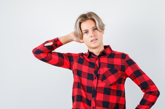 Teen Boy im karierten Hemd mit der Hand hinter dem Kopf und wehmütig, Vorderansicht.