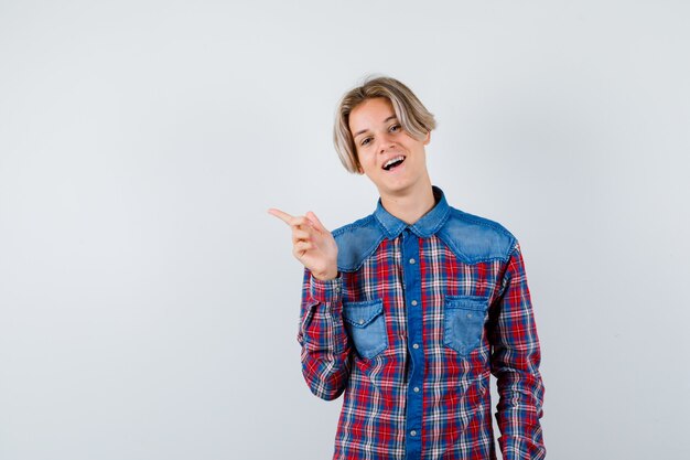 Teen Boy im karierten Hemd zeigt auf die obere linke Ecke und sieht fröhlich aus, Vorderansicht.